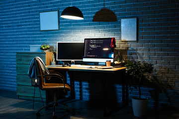 Interior of dark programmer's office with workplace and glowing lamp