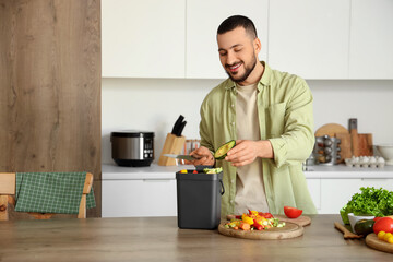 Young man with compost bin and vegetable scraps during cooking in kitchen