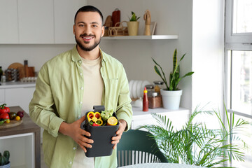 Young man with compost bin and vegetable scraps during cooking in kitchen
