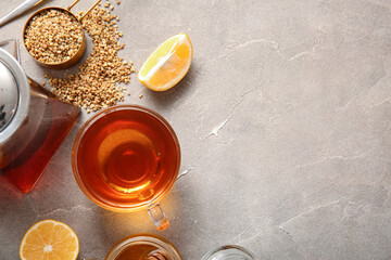 Glass cup and teapot of hot buckwheat tea with lemon on grey background