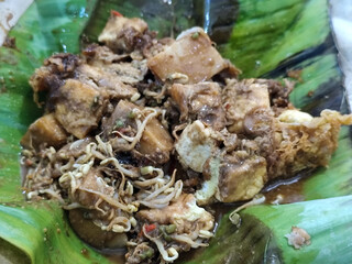 Tahu lontong, a delicious traditional Indonesian dish, lontong with peanut sauce, soy sauce, served with pieces of side dish on banana leaves.
