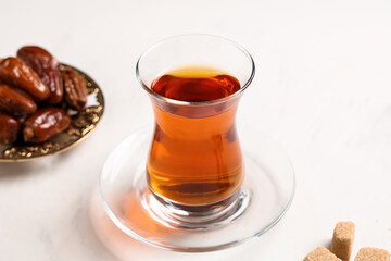 Glass of Turkish tea with sugar cubes and dried dates on white background