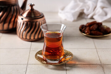 Glass of Turkish tea with pot and dried dates on white tile table