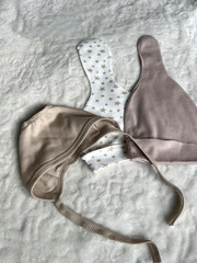 Beige and white caps with stars, a cap are lying on a light plaid bed in the room. A set of...