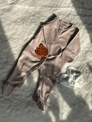 A dark beige suit for a newborn is lying in the sun on a white bedspread. Preparation for discharge...
