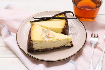 Plate with pieces of sweet vanilla cheesecake and glass cup of tea on white wooden background