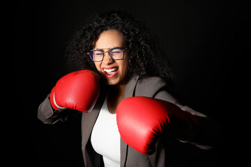 Emotional African-American businesswoman with boxing gloves on dark background. Knockout concept