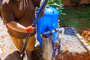Plumber worker connects hoses to new artesian water well filtration system in residential area...