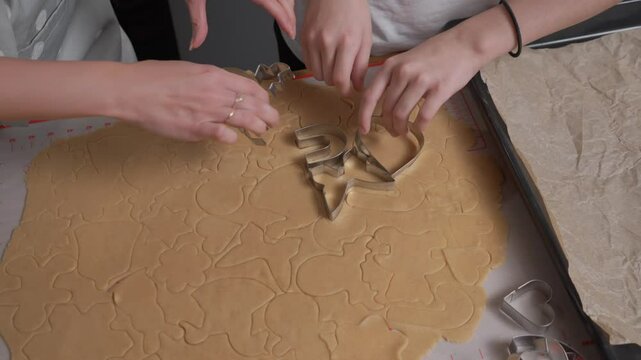 Hands carefully lift and remove metal cookie cutters one by one from the rolled-out dough. This reveals a pattern of perfectly cut, raw gingerbread cookie shapes ready to be baked.