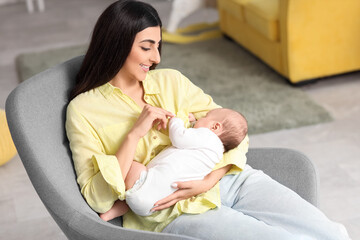 Woman breastfeeding her baby while sitting in armchair at home