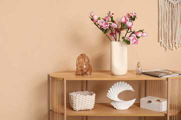 Vase with blooming magnolia flowers on console table near beige wall