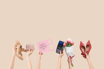 Female hands holding shoes with postcard, payment terminal and flowers on beige background....