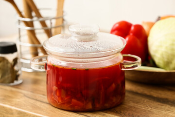 Glass pot with tasty borscht and ingredients for preparing on table in kitchen