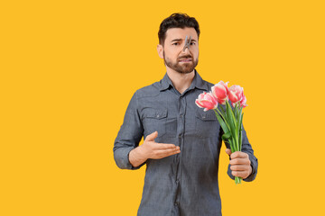 Ill young man with clothespin on his nose and tulip flowers against yellow background. Stuffy nose...