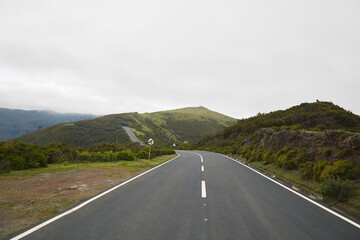 Winding asphalt road curving through a green mountain landscape under a cloudy sky
