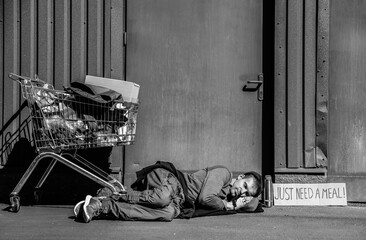 Homeless man with shopping cart and cardboard sleeping on street