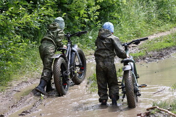 Boys in waterproof clothes and rubber boots ride fatbikes. A fat bike for off-road use