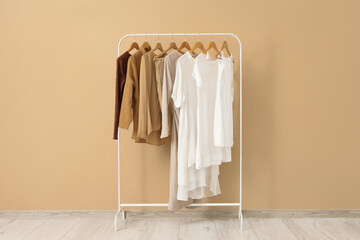 Rack with stylish clothes near beige wall in room