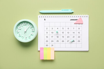 Calendar with alarm clock, stationery and sticky notes on green background. Planning concept