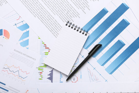 Notebook with pen, many business documents and graphics as background, closeup