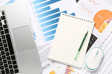 Laptop with computer mouse, notebook, many business graphics and diagrams as background, closeup