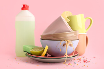 Dirty dishes with detergent and sponge on pink background