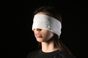 Young woman with blindfold on black background. Concept of oppression