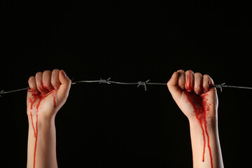 Hands with blood and barbed wire on black background. Concept of oppression
