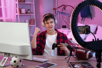 Teenage blogger with game pad recording video at table in bedroom