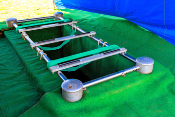 During burial ceremony, silver coffin holder is placed over freshly dug grave, surrounded by...