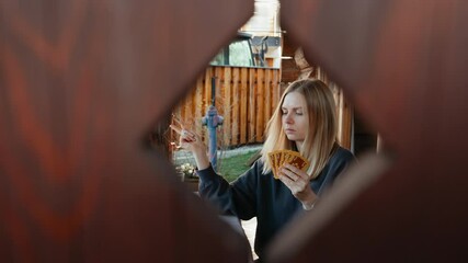 Young blonde woman enjoying card game on cozy terrace, casually dancing while drawing playing card from deck. playing cards inspire leisure. Concept of tabletop games, leisure, and emotional joy. 