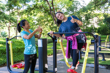 Plus size sportswoman doing exercise with machine in playground gym park with female trainer taking...