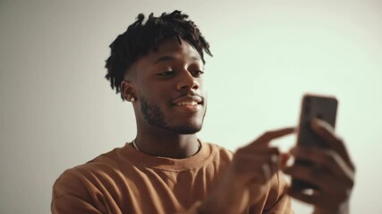 Young african american man browses social media on phone. Guy uses mobile app, online communication, digital lifestyle footage. - Powered by Adobe