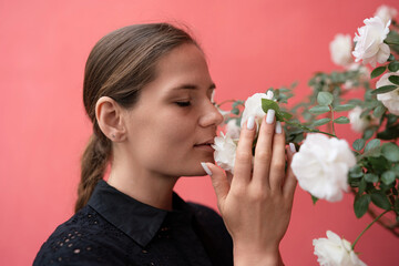Woman Roses Aroma: Young woman smelling white roses, with closed eyes, indoors, on coral background, for pleasure.