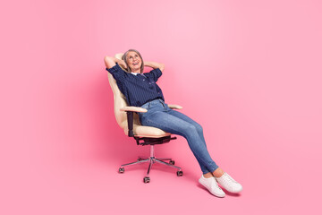 Fototapeta premium Confident mature woman relaxing on a chair against a vibrant pink background in casual attire radiating joy