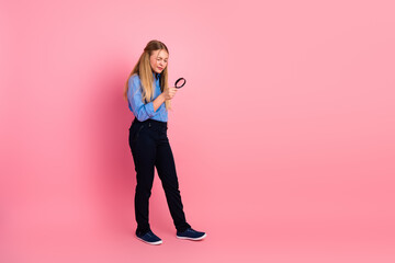 Smiling young girl holding a magnifying glass against vibrant pink background representing...
