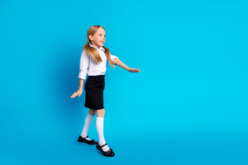 Happy young schoolgirl walking in uniform on blue background, smiling and showing playful gestures, representing education