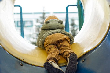 The boy slides down the bright tube slide and laughs happily. A walk on the playground in the cold...