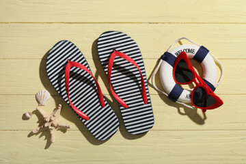 Stylish flip-flops, sunglasses and decorative lifebuoy on beige wooden background
