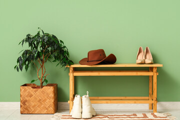 Stylish felt hat with shoes on bench near green wall in hallway