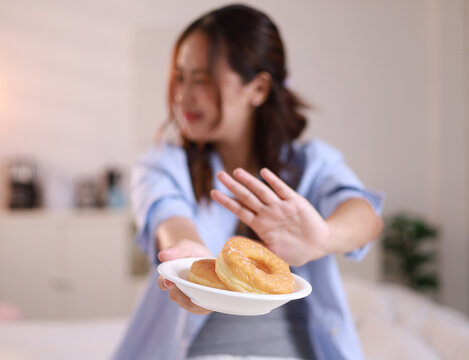 Young woman pushes hand away, rejects sugary donuts, donuts and sweets on plate, weight loss concept, healthy weight loss
