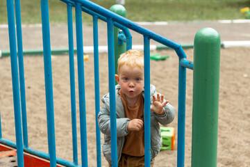 Obraz premium Portrait of a little red-haired boy who looks over the fence of a playground. Fun outdoor walks