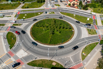 Large roundabout intersection with greenery and road markings surrounded by vehicles and urban roads