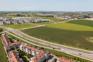 Fototapeta premium Sprawling suburban housing with fields and cityscape in the distance under clear summer sky