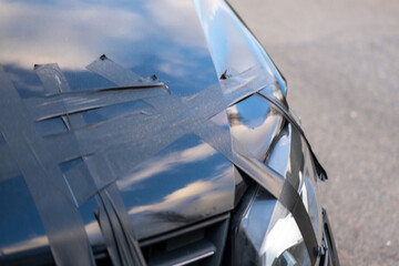 damaged black car after crash, hood taped with duct tape, scratched surface, Urban accident detail,...