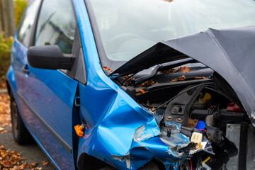 heavily damaged car with crumpled hood and exposed engine, aftermath collision, crash scene, with...