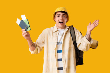 Happy male tourist with passports and backpack on yellow background