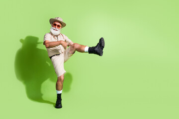 Mature adventurer posing confidently in safari-style attire against a green backdrop during an...