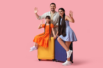 Fototapeta premium Family of tourists with suitcases waving hands on pink background