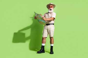Photo of amazed traveler man hold map lost in wild nature wear safari suit isolated green color...